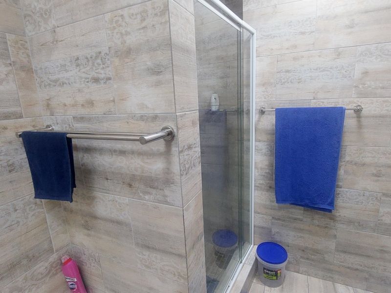 A modern bathroom featuring neutral wood-look ceramic wall tiles and a glass-enclosed shower stall with chrome towel rails.