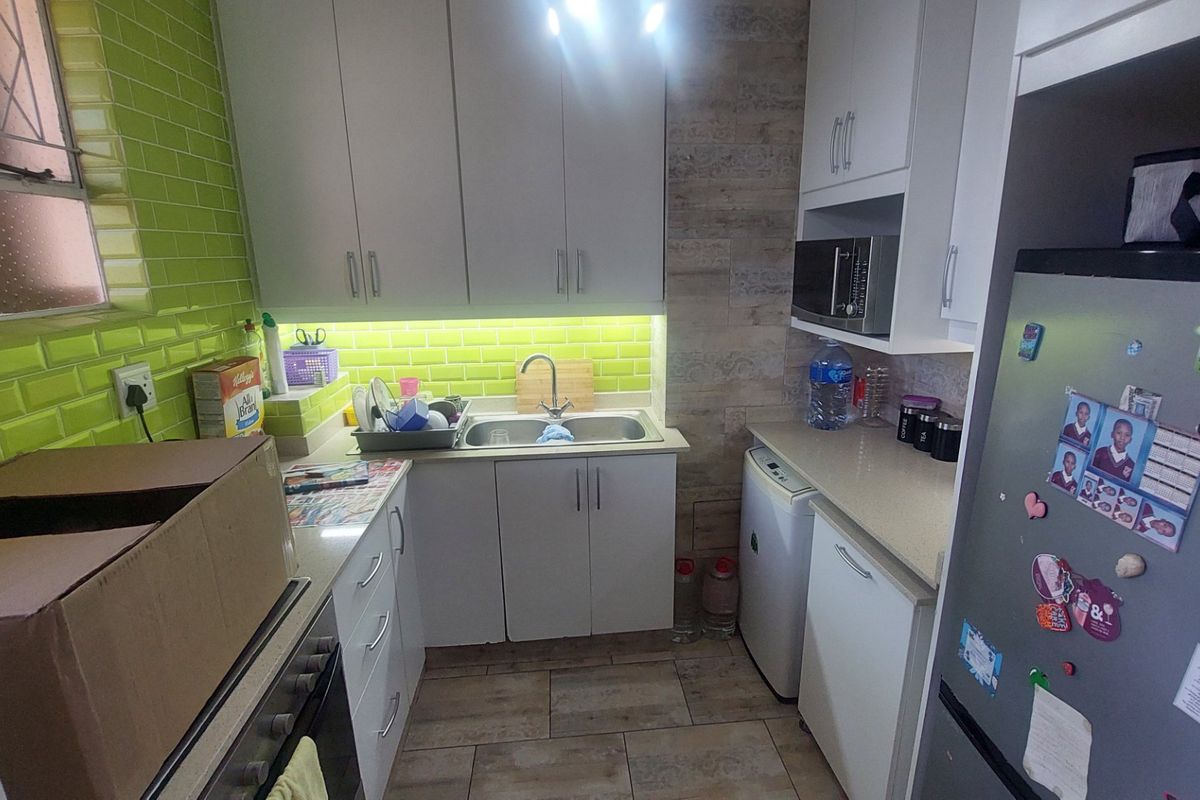 Compact kitchen featuring white cabinetry, stone countertops, a vibrant green subway tile backsplash, and integrated appliances including an oven and microwave.
