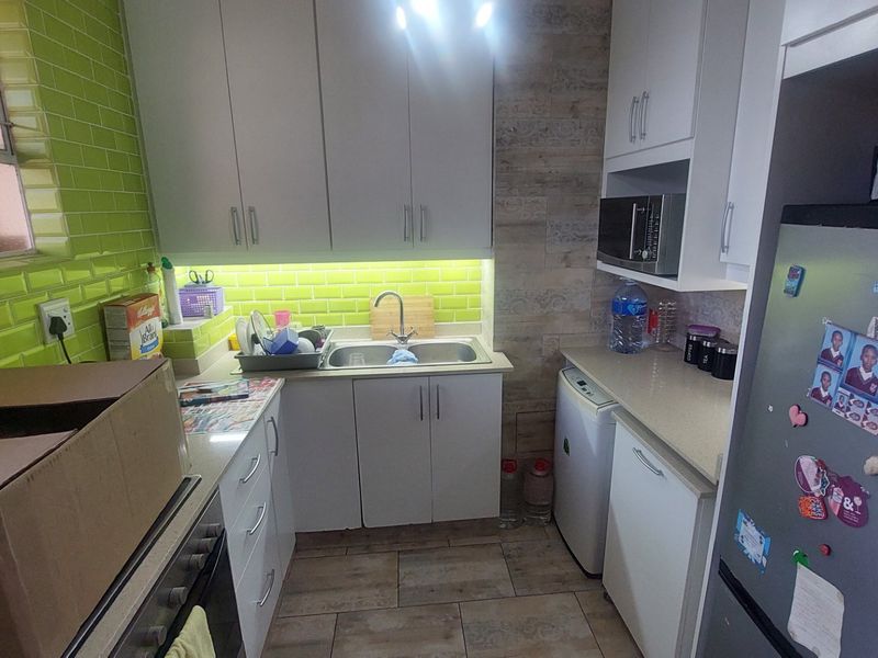 Compact kitchen featuring white cabinetry, stone countertops, a vibrant green subway tile backsplash, and integrated appliances including an oven and microwave.