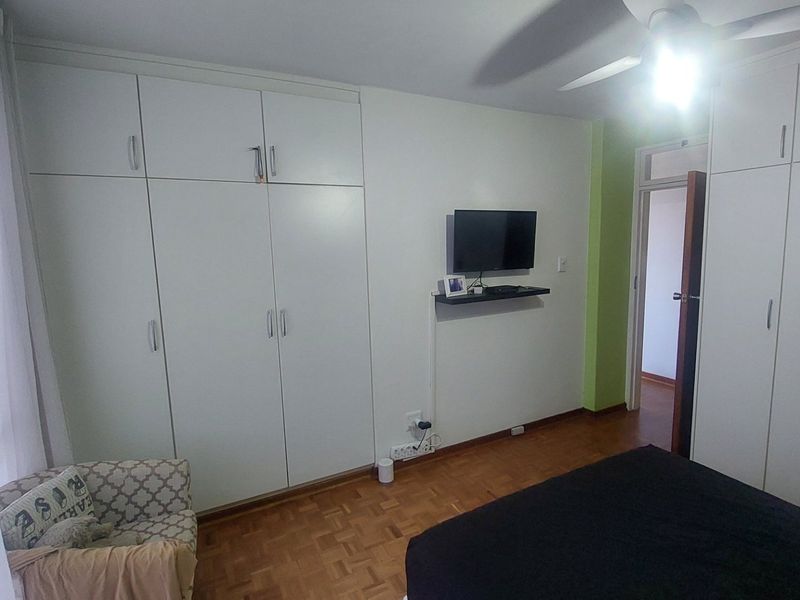 Bedroom featuring extensive built-in cupboard storage, parquet flooring, and a ceiling fan, providing a functional and practical living space.
