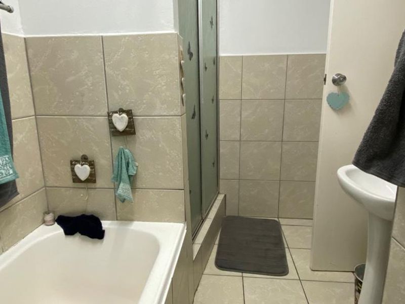 A functional bathroom featuring a bathtub, a separate shower enclosure, and a pedestal sink with neutral ceramic wall and floor tiling.