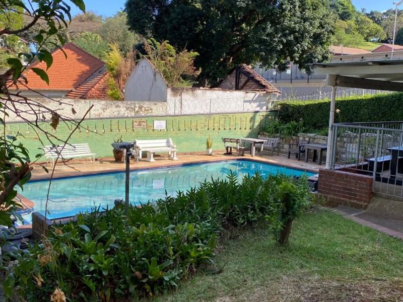 Outdoor pool area featuring a swimming pool, paved surround, and a covered patio space, set within a private garden with boundary walling.