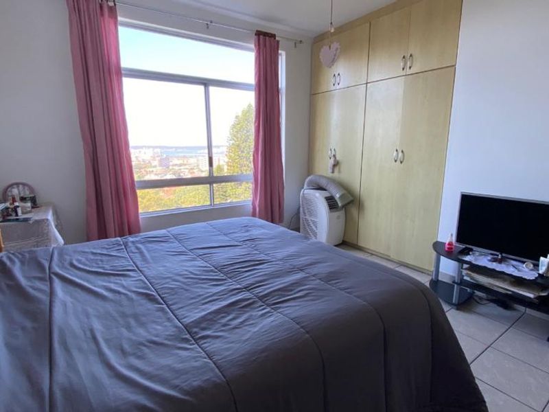 A bedroom featuring built-in cupboards, tiled flooring, and a large window offering natural light and elevated views.