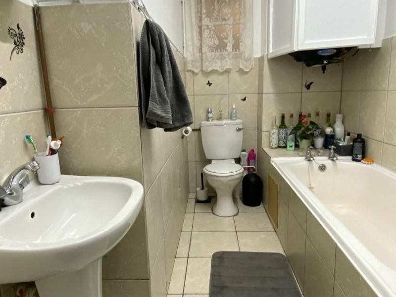 A functional bathroom featuring a pedestal washbasin, standard toilet, and a bathtub with full-height wall tiling.