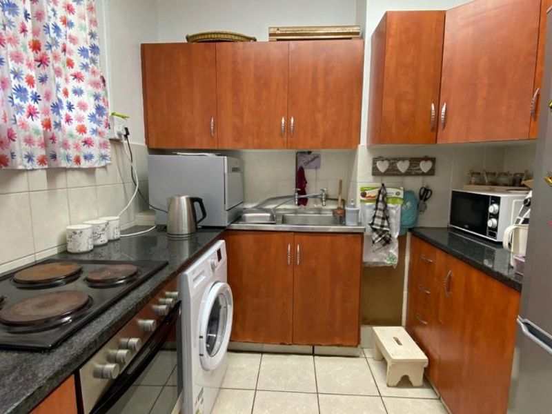 Compact kitchen featuring wood-look cabinetry, dark laminate countertops, tiled backsplash, and integrated electric cooking appliances.