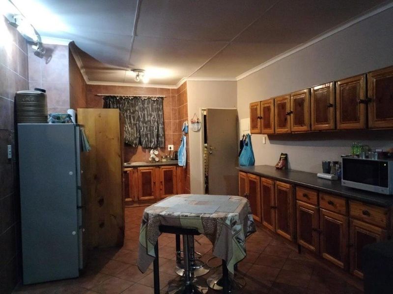 A dated kitchen featuring wooden cabinetry, laminate countertops, and tiled flooring. The space offers functional storage and preparation areas in need of modernization.