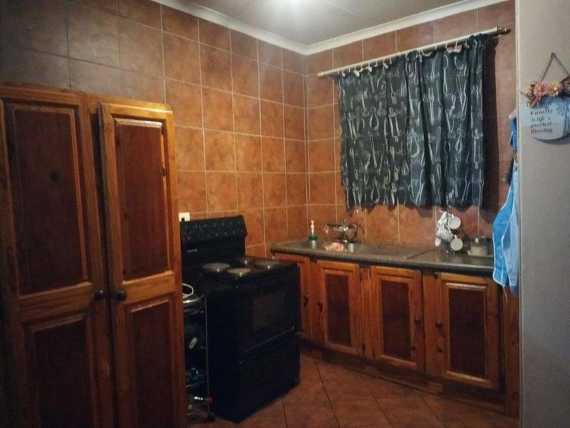 A functional kitchen featuring wooden cabinetry, tiled backsplash, and tiled flooring, providing a traditional layout with a freestanding stove and sink area.