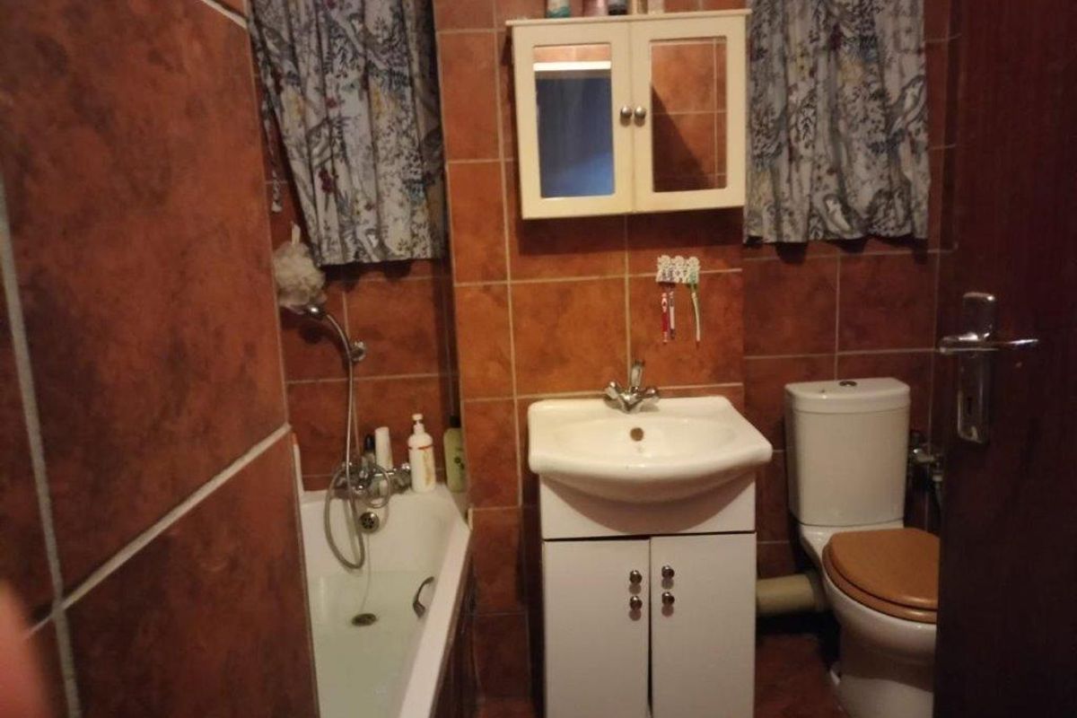 A compact bathroom featuring a bathtub, vanity washbasin, and toilet with full-height wall tiling.