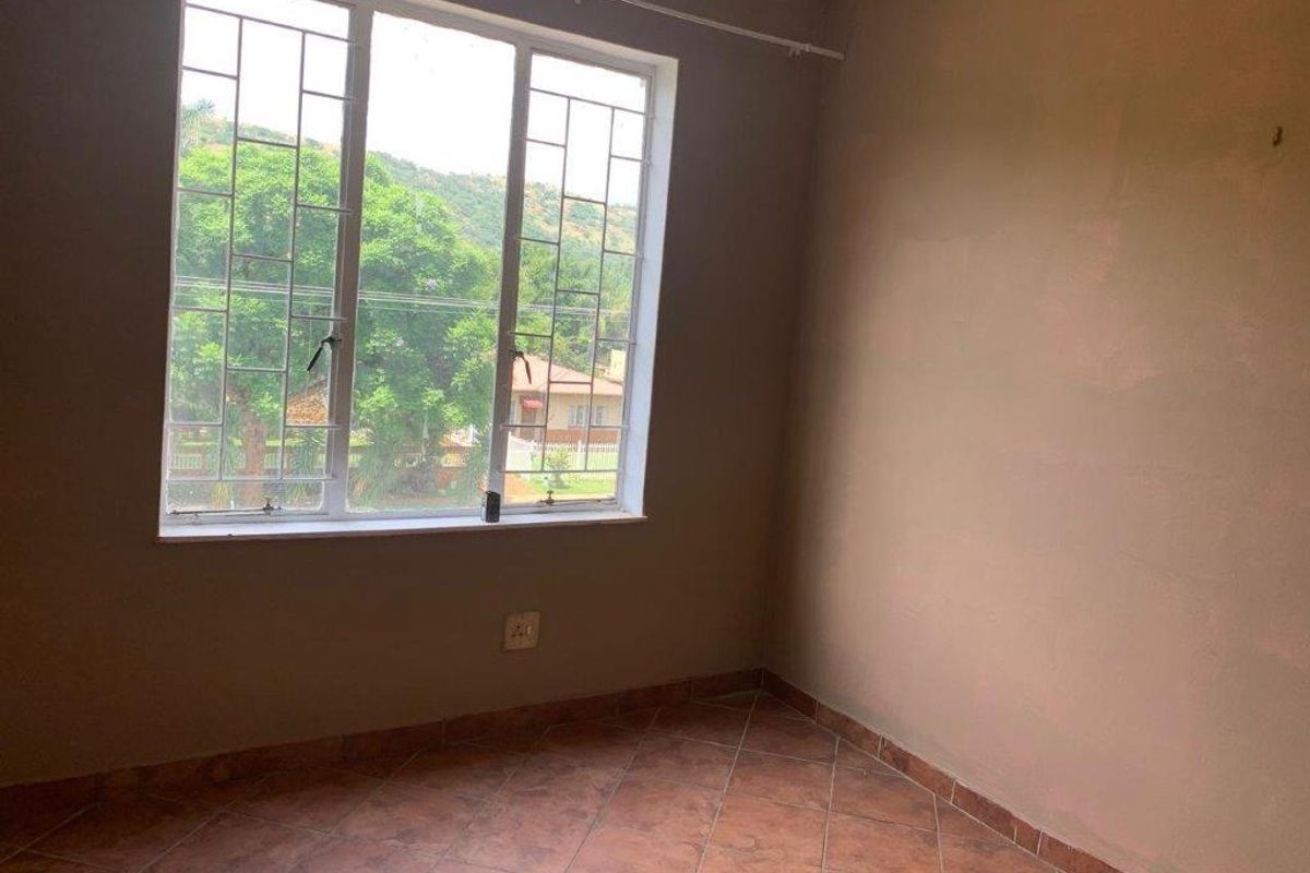 An empty bedroom featuring tiled flooring, a large window with security bars, and neutral wall finishes, offering a blank canvas for personalization.