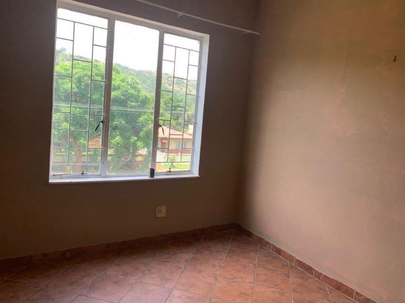 An empty bedroom featuring tiled flooring, a large window with security bars, and neutral wall finishes, offering a blank canvas for personalization.