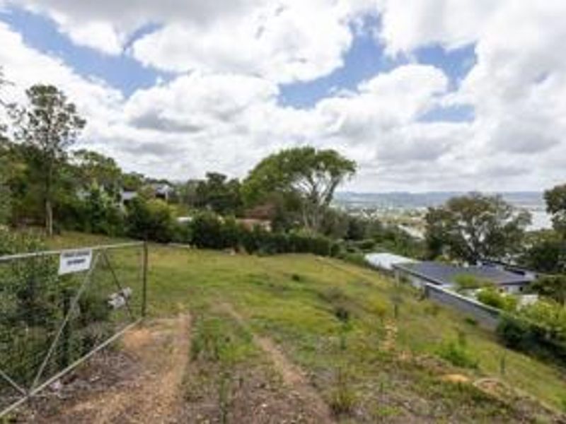 A sloped residential vacant land plot featuring established trees, perimeter fencing, and a metal gate, offering potential for development with scenic views.