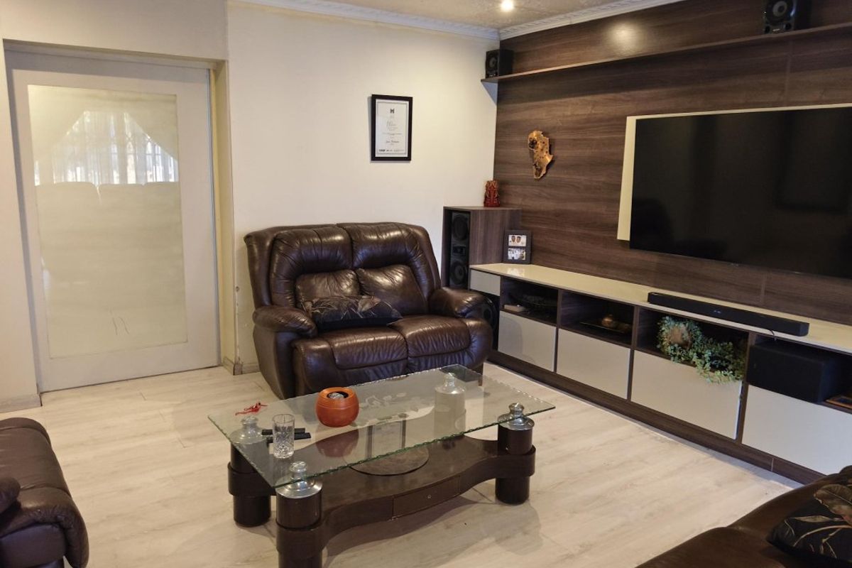 A comfortable living room featuring a modern built-in media wall unit, light-toned laminate flooring, and a decorative coved ceiling.
