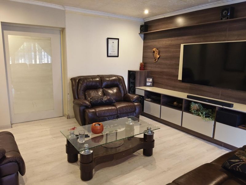A comfortable living room featuring a modern built-in media wall unit, light-toned laminate flooring, and a decorative coved ceiling.