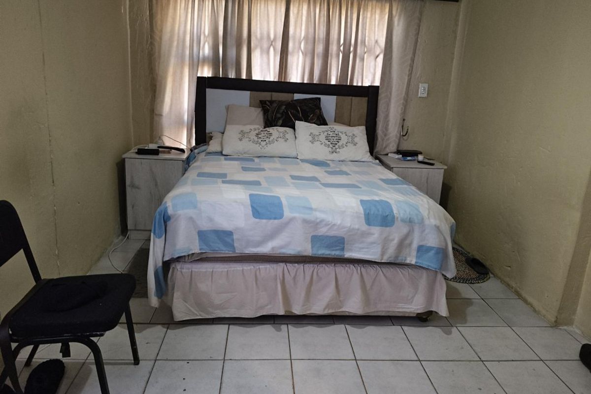 A bedroom featuring tiled flooring and a window with a security gate, requiring cosmetic updates to improve the overall finish and appeal.