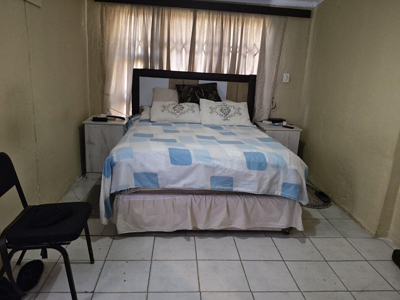 A bedroom featuring tiled flooring and a window with a security gate, requiring cosmetic updates to improve the overall finish and appeal.