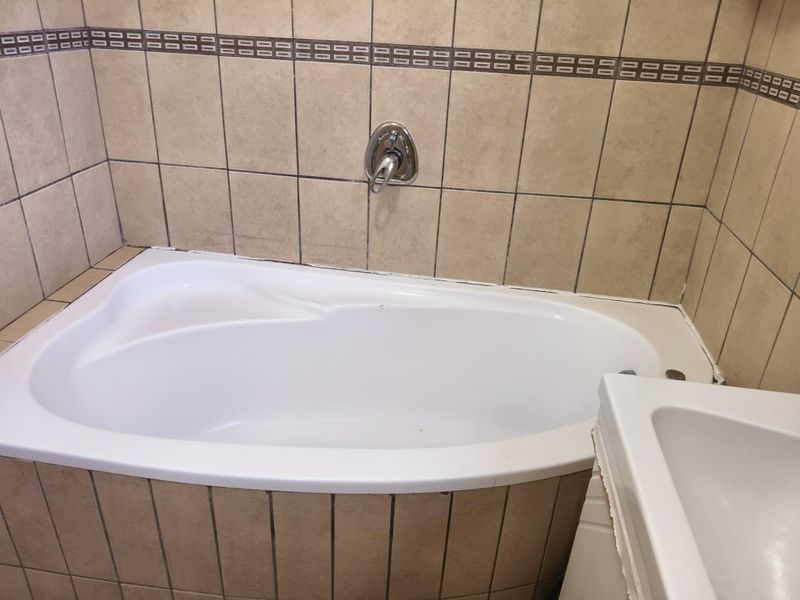 A bathroom featuring a built-in bathtub with wall-mounted mixer tap and neutral ceramic wall tiling.
