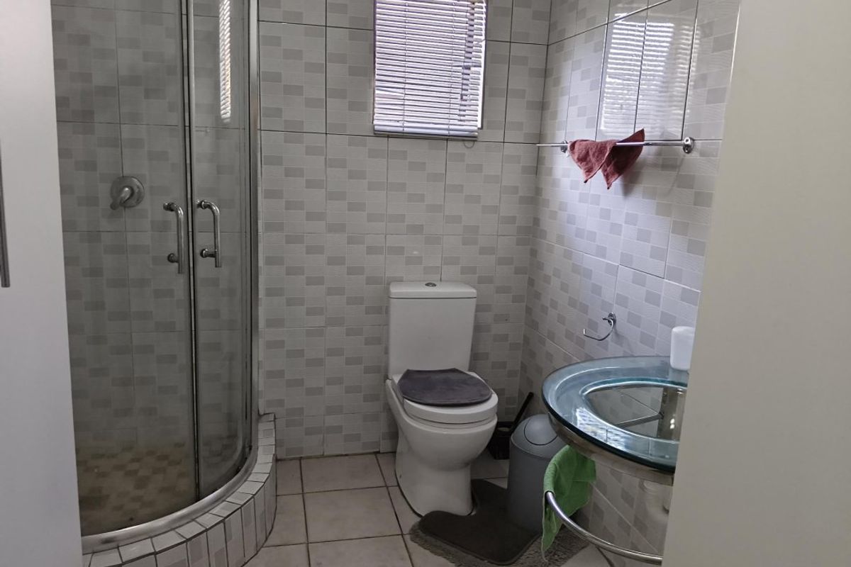 A functional bathroom featuring a glass shower enclosure, a modern glass vanity basin, and neutral wall and floor tiling.