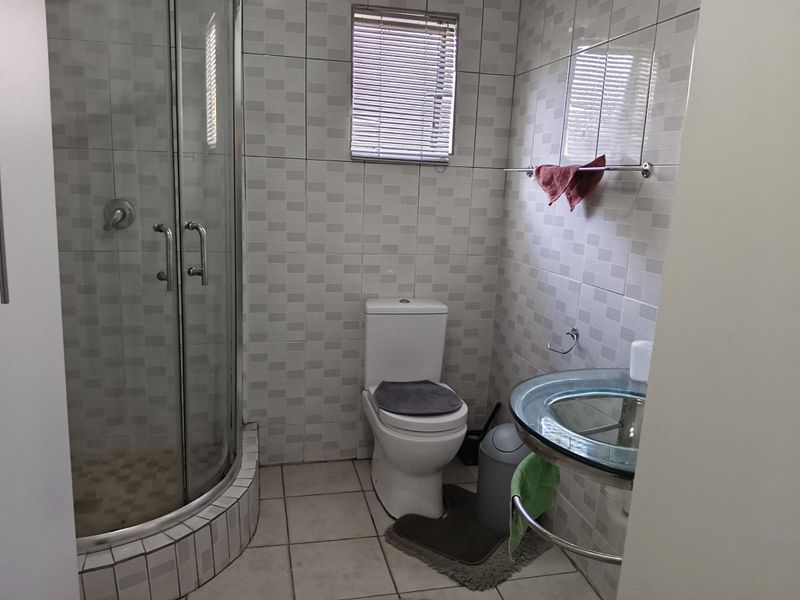 A functional bathroom featuring a glass shower enclosure, a modern glass vanity basin, and neutral wall and floor tiling.