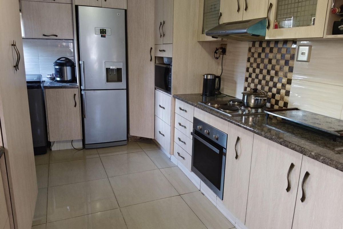 A functional kitchen featuring light wood-finish cabinetry, granite countertops, a built-in oven, electric hob, and tiled flooring.