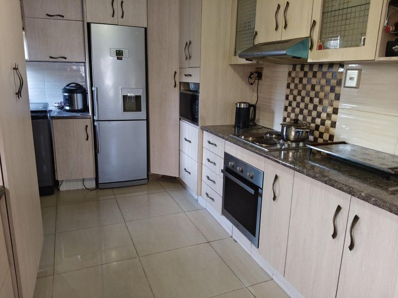 A functional kitchen featuring light wood-finish cabinetry, granite countertops, a built-in oven, electric hob, and tiled flooring.