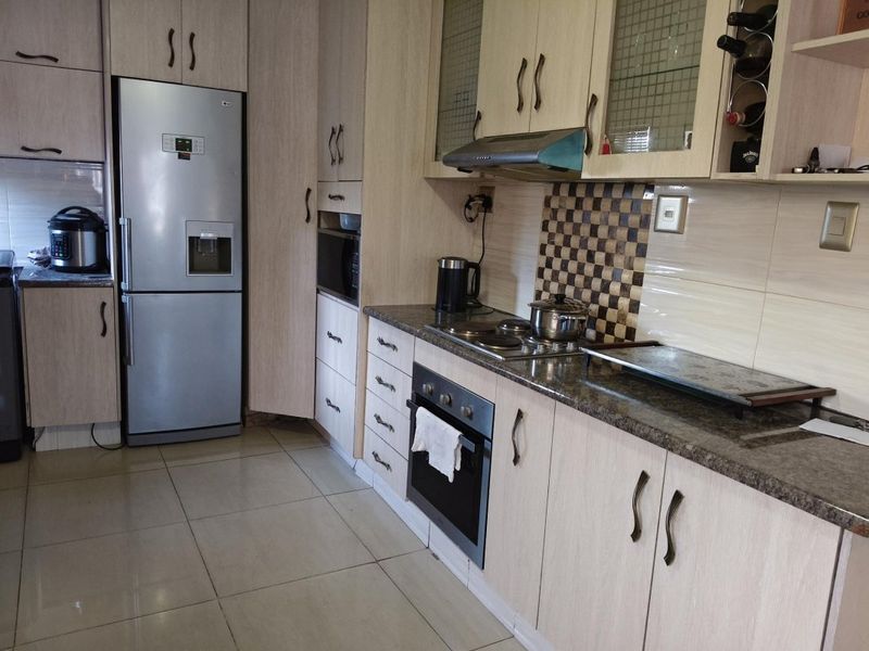 A functional kitchen featuring light wood-finish cabinetry, granite countertops, a tiled backsplash, and integrated appliances including an oven and hob.
