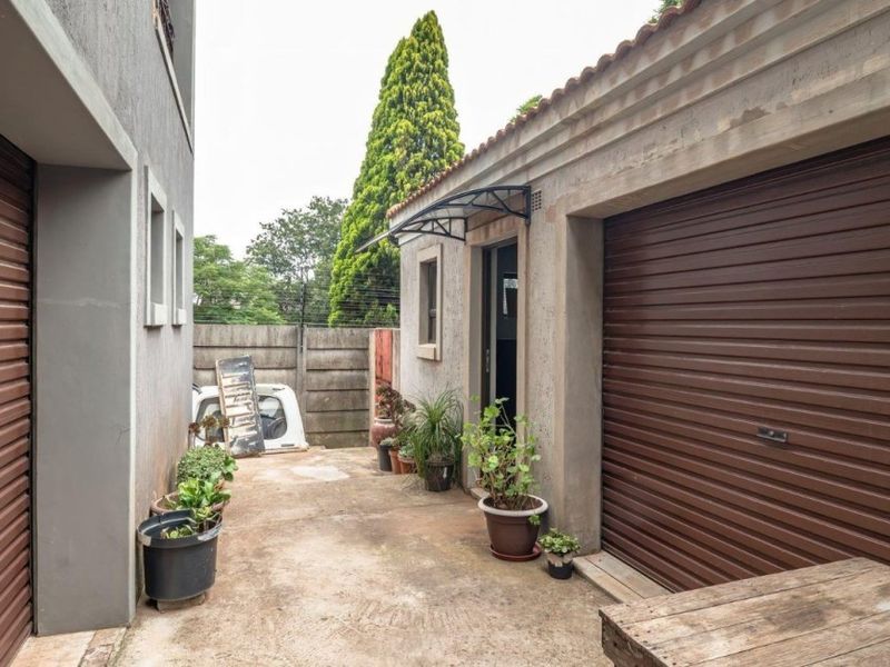 A side passage area between two structures featuring roller garage doors, concrete paving, and a small protective awning over the entrance.