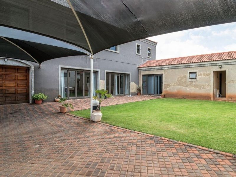 Rear exterior view featuring a paved driveway, shade sail, lawn, and access to the garage and main dwelling via sliding glass doors.
