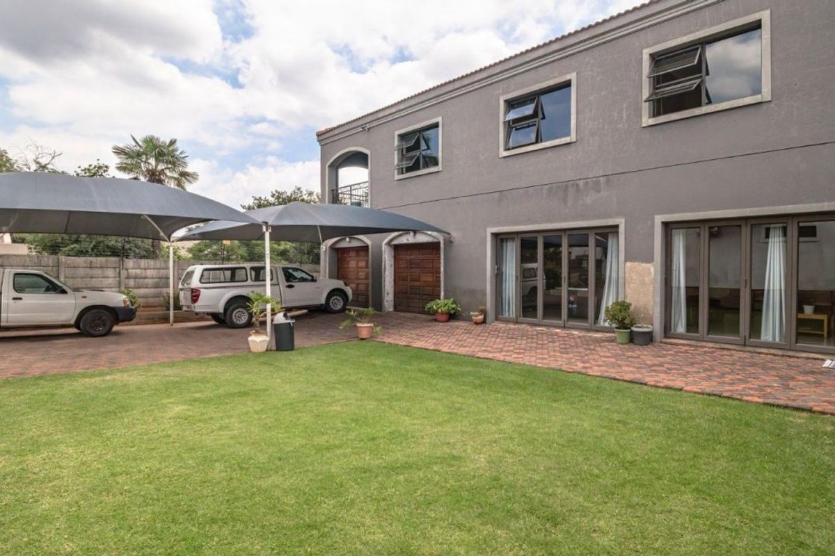 Rear exterior view of a two-story house featuring a paved driveway, shade sail carport, lawn, and multiple sliding glass door access points.
