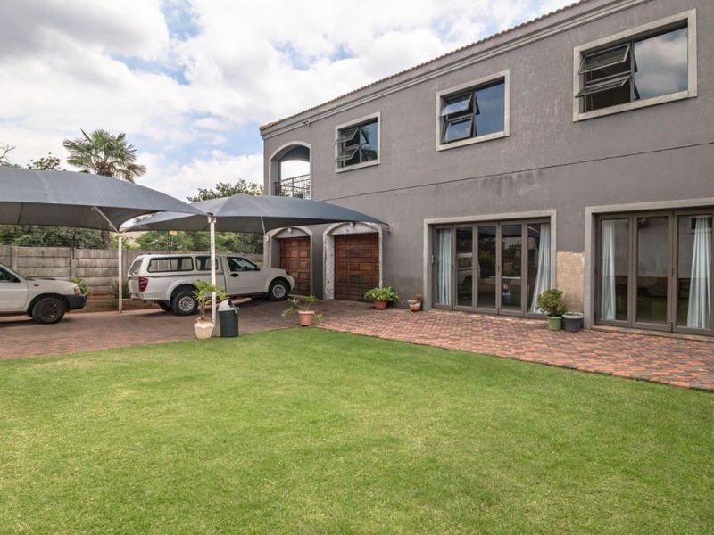 Rear exterior view of a two-story house featuring a paved driveway, shade sail carport, lawn, and multiple sliding glass door access points.