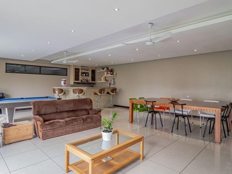 Spacious open-plan living and entertainment area featuring a built-in bar, recessed lighting, ceiling fans, and large format floor tiles throughout.