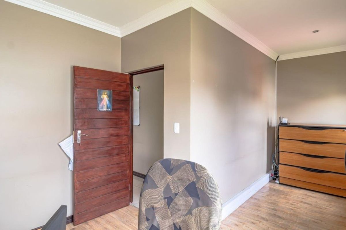 A bedroom featuring laminate flooring, crown molding, and a solid wood door leading to an adjacent space.