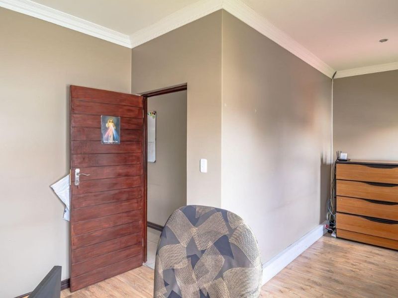 A bedroom featuring laminate flooring, crown molding, and a solid wood door leading to an adjacent space.