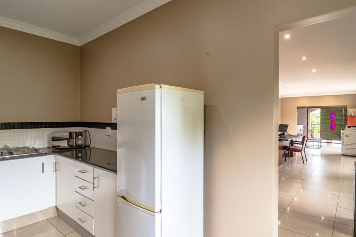 A functional kitchen area featuring white cabinetry, granite countertops, and a tiled backsplash, leading into an open-plan living space with tiled floors.