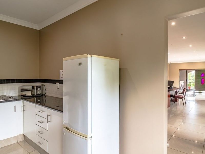 A functional kitchen area featuring white cabinetry, granite countertops, and a tiled backsplash, leading into an open-plan living space with tiled floors.