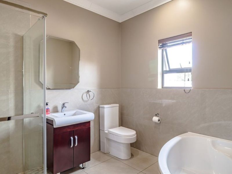 A well-maintained bathroom featuring a glass shower enclosure, a bathtub, a vanity cabinet with a basin, and neutral wall tiling.