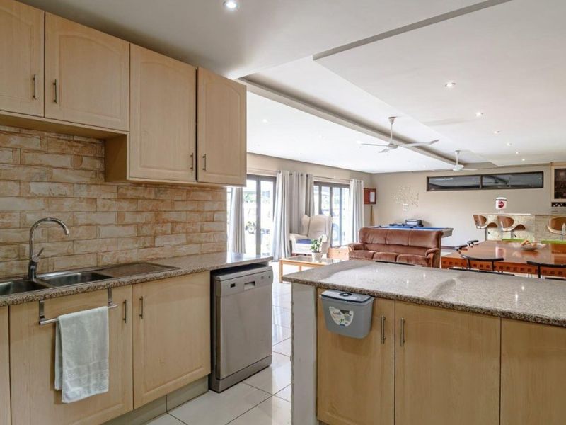 Spacious open-plan kitchen and living area featuring granite countertops, stone veneer backsplash, and ample cabinetry, flowing into a versatile entertainment space.