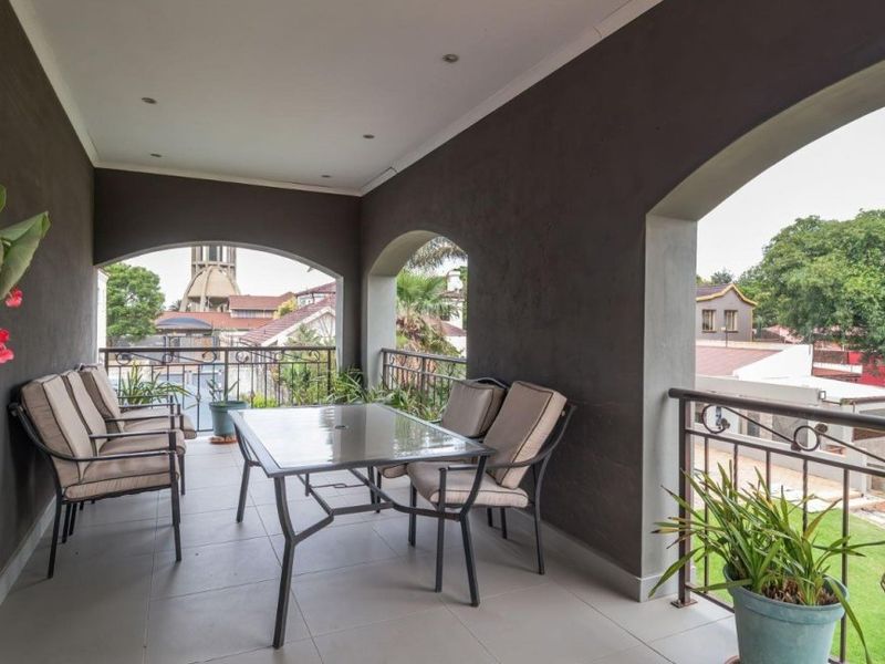 A covered balcony featuring tiled flooring, recessed lighting, and arched structural openings, offering an elevated view of the surrounding neighborhood.