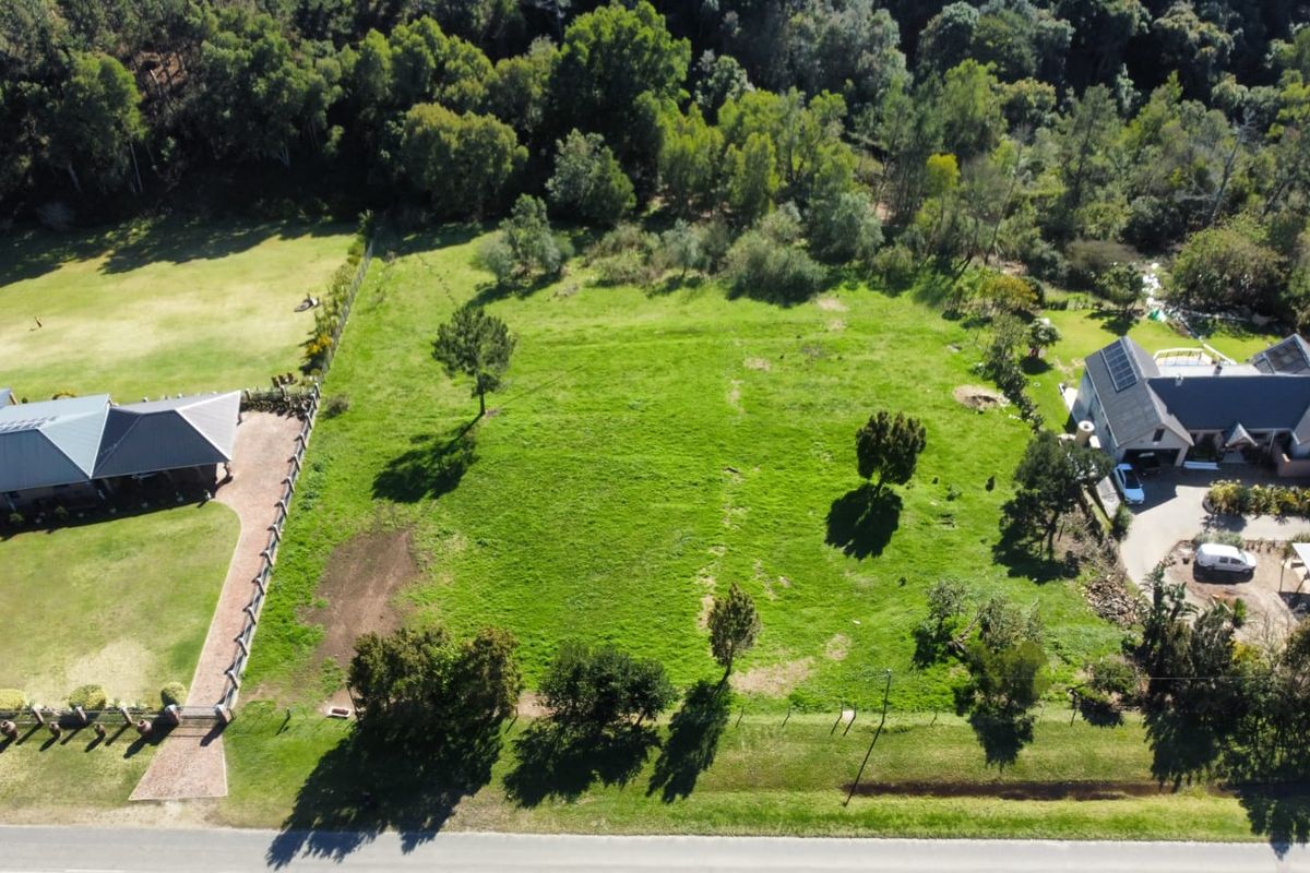 An aerial view of a vacant residential plot featuring established trees, grassed terrain, and perimeter fencing, situated between existing residential properties.