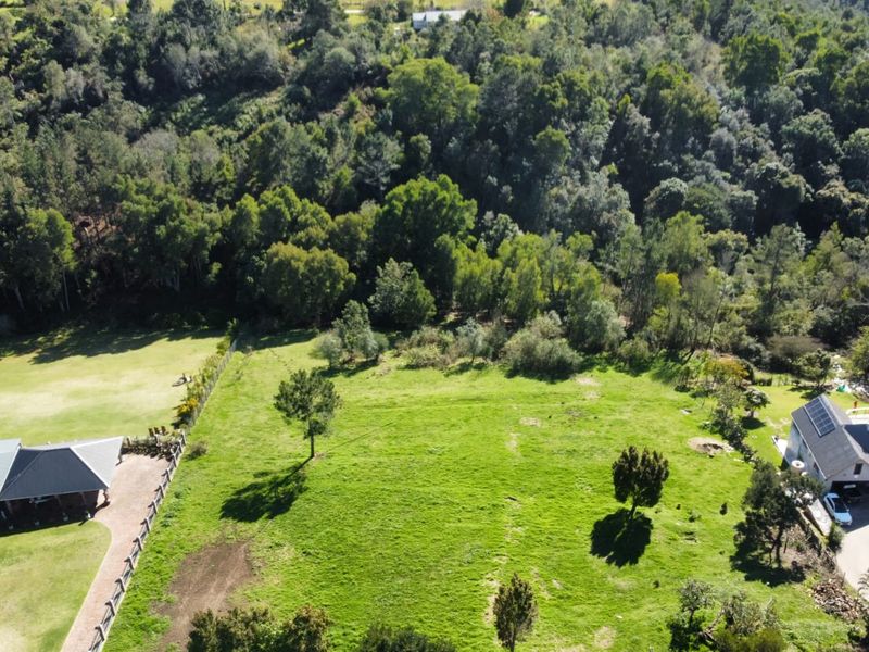 Aerial view of a large, well-maintained residential vacant land plot featuring established trees and fenced boundaries, situated in a scenic, green environment.