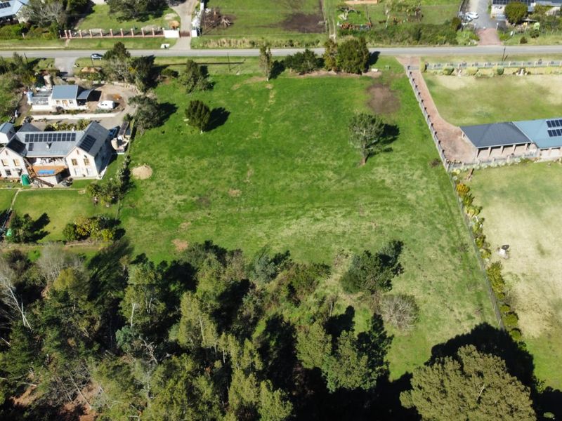 An aerial view of a vacant residential plot featuring established trees and perimeter fencing, situated in a developed neighborhood.