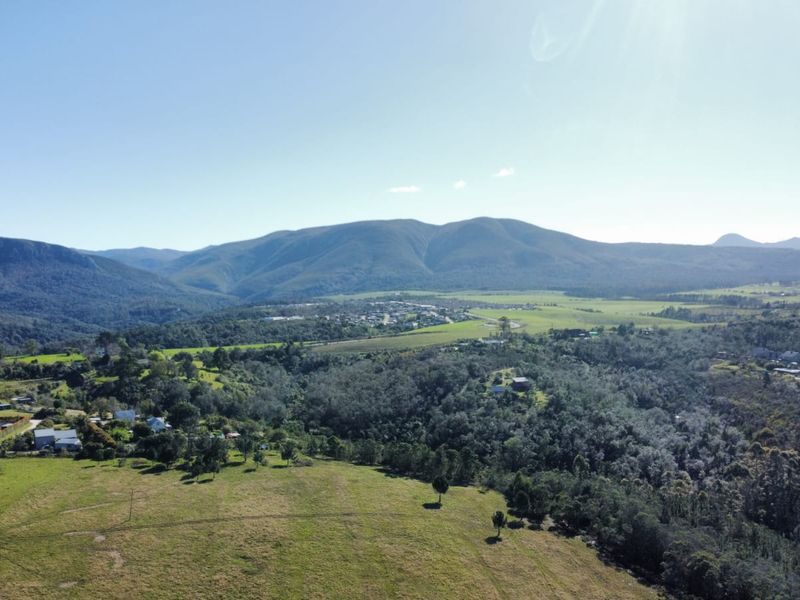 An expansive aerial view of the surrounding landscape, featuring rolling hills, dense vegetation, and a scenic mountain range in the distance.