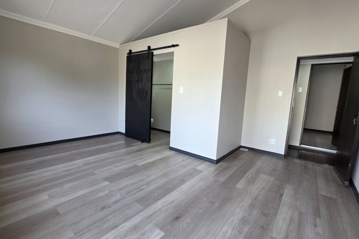 A spacious, empty bedroom featuring modern laminate flooring, a stylish black sliding barn door, and neutral wall finishes.