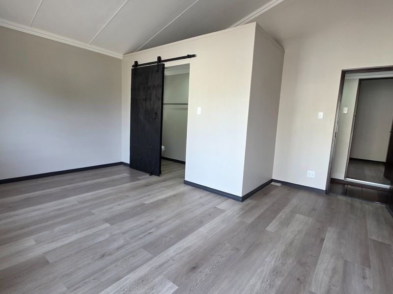 A spacious, empty bedroom featuring modern laminate flooring, a stylish black sliding barn door, and neutral wall finishes.