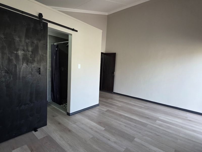 A spacious, empty bedroom featuring modern laminate flooring, a stylish black sliding barn door, and access to an en-suite bathroom.