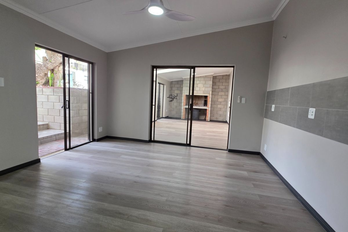 Spacious living area featuring modern laminate flooring, neutral walls with tiled accents, and sliding glass doors providing access to an outdoor patio space.