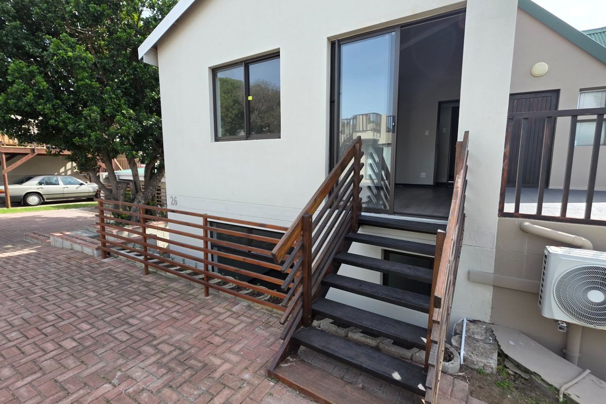 Rear exterior view featuring a paved area, timber staircase with balustrade, sliding glass door access, and an external air conditioning unit.