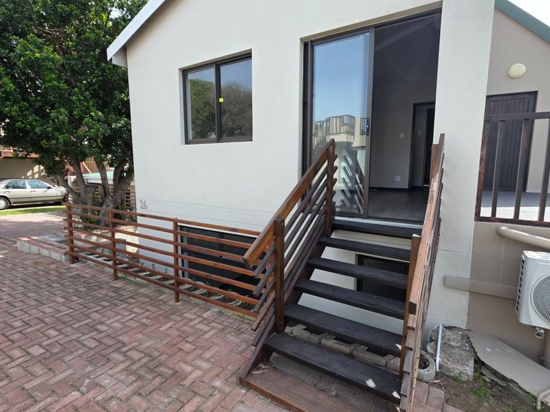 Rear exterior view featuring a paved area, timber staircase with balustrade, sliding glass door access, and an external air conditioning unit.