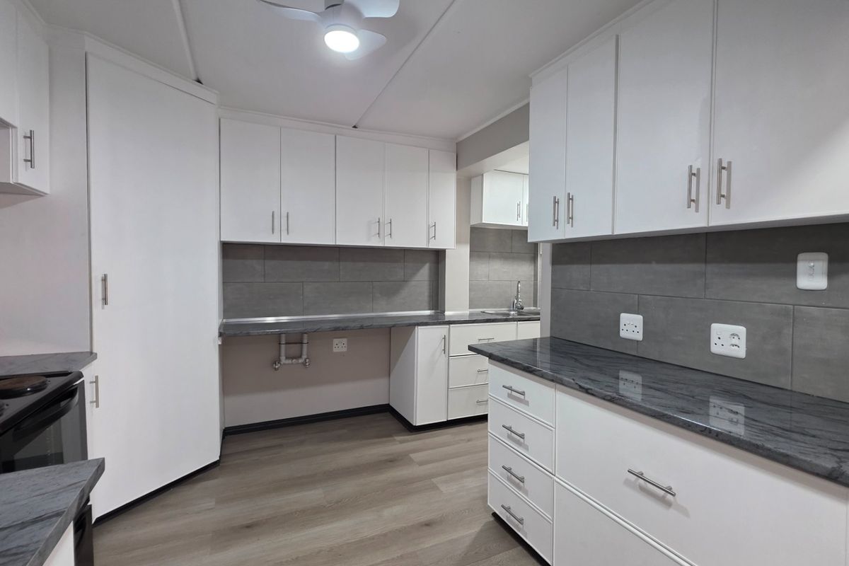 Modern kitchen featuring white cabinetry, dark stone countertops, grey tiled backsplash, and integrated electric stove, offering a clean and functional workspace.