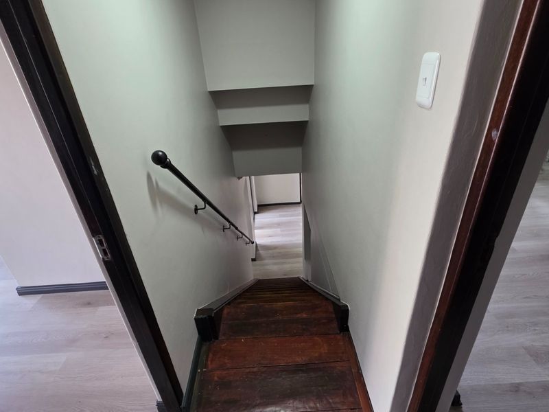 A view looking down a wooden staircase with a metal handrail, connecting two levels with light-toned laminate flooring.