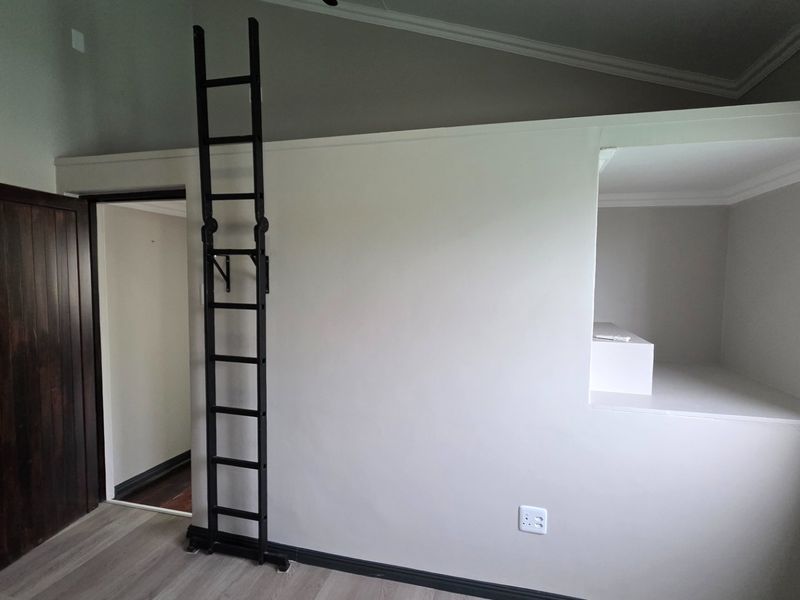 Bedroom featuring a built-in loft sleeping area accessed by a fixed metal ladder, with neutral walls and timber door.